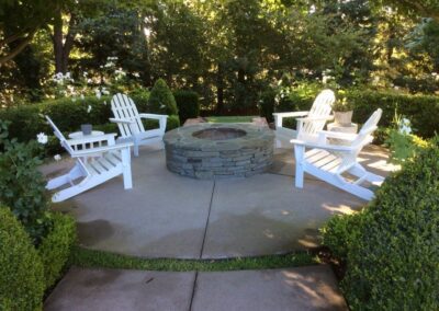 white adirondack chairs around a round stone firepit